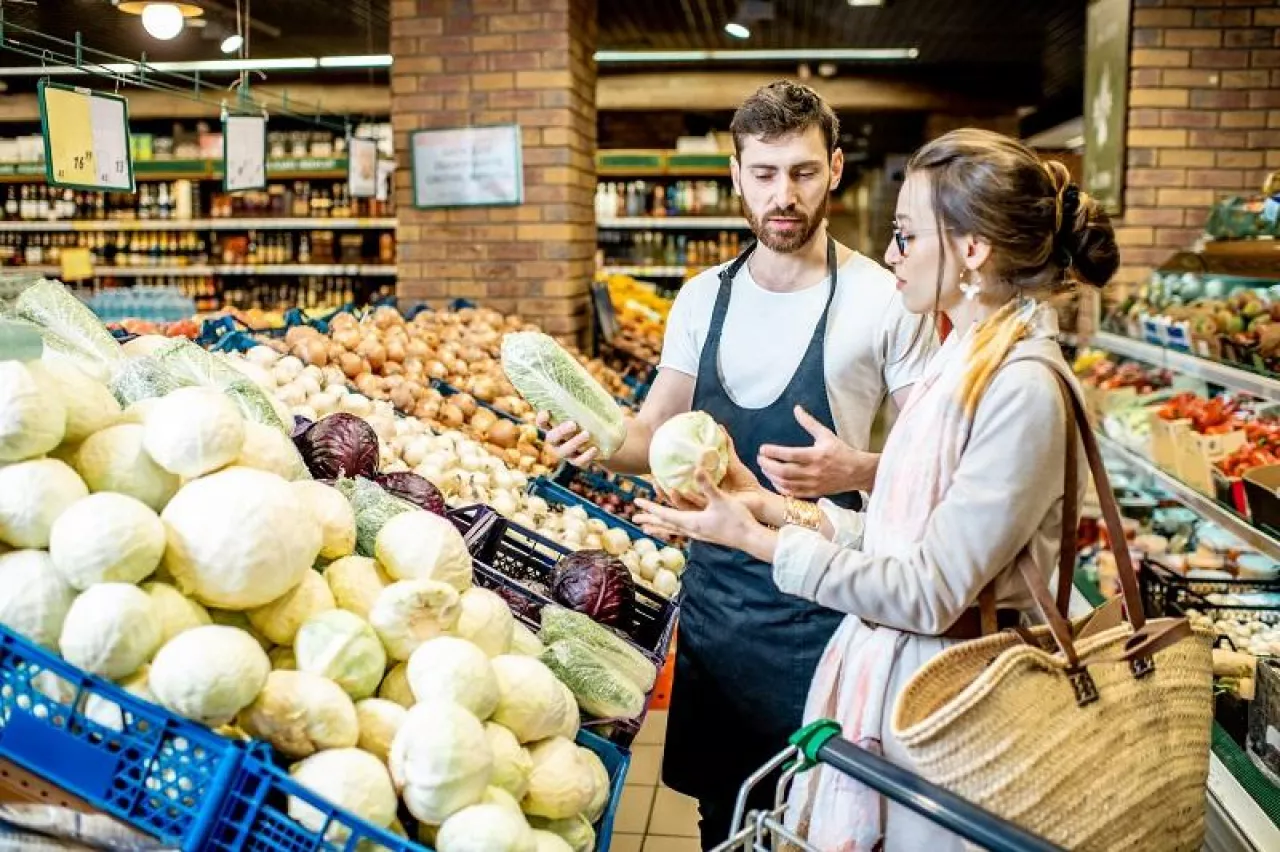 Shop worker helping young woman client to chooose vegetables in the supermarket