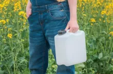 Rapeseed crop protection concept, female farmer agronomist holding jerry can bottle container with pesticide, selective focus