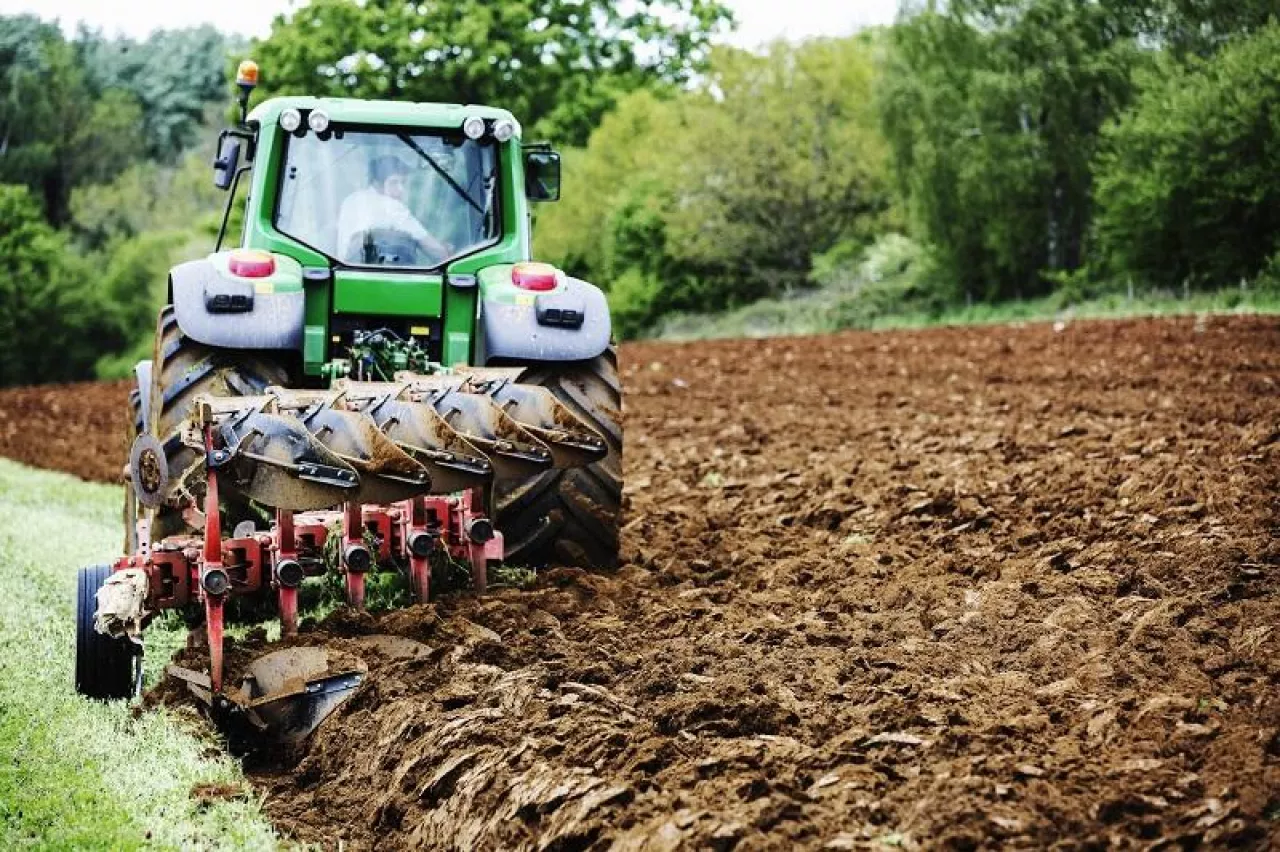 A tractor ploughing the soil in a field, harrowing.