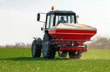 Unrecognizable farmer in agricultural tractor is fertilizing wheat crop field with NPK fertilizer nutrients