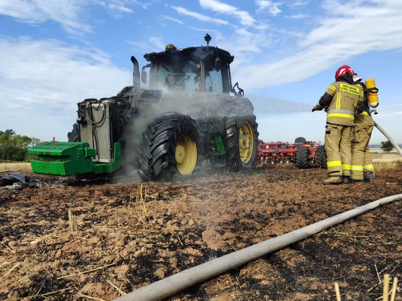 Strażacy dogaszają palący się ciągnik na polu