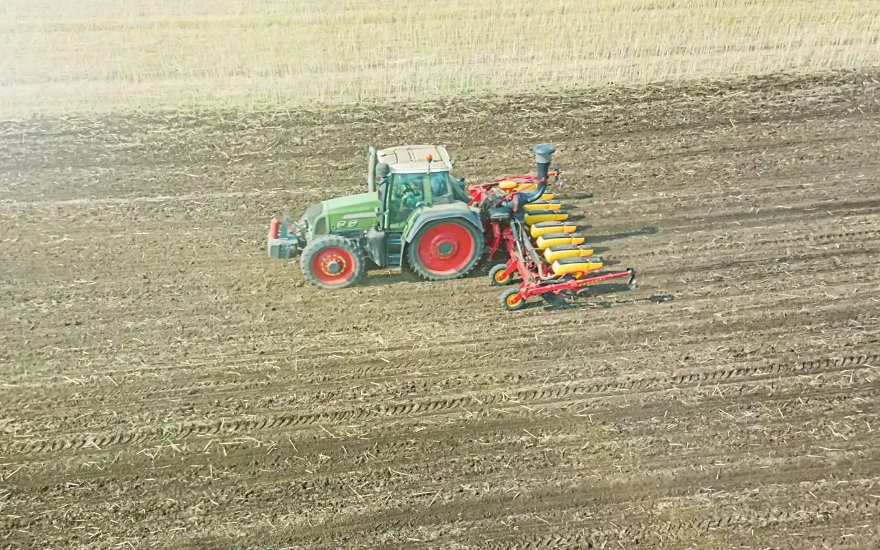 Traktor wykonuje siew na dużym polu uprawnym. Zdjęcie z drona przedstawia pracę maszyn rolniczych podczas wiosennych lub jesiennych zasiewów