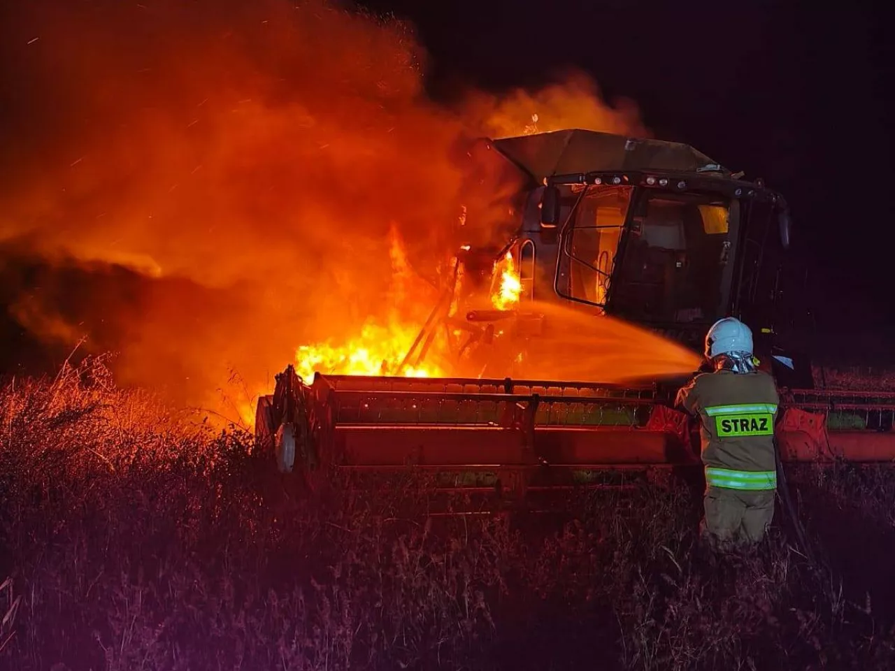Strażak nocną porą gasi pożar kombajnu na polu