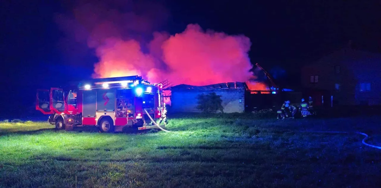 Czerwony wóz gaśniczy straży pożarnej przed palącą się stodołą