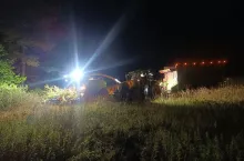 Sieczkarnia oraz ciągnik rolniczy z przyczepą podczas nocnych prac polowych na polu kukurydzy