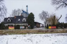 Budynek mieszkalny, a za nim gospodarstwo rolne, a na płocie wywieszone banery sprzeciwiające się budowie CPK