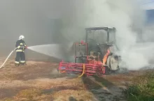 Strażak w czarnym nomexie gasi pożar ciągnika rolniczego z opryskiwaczem