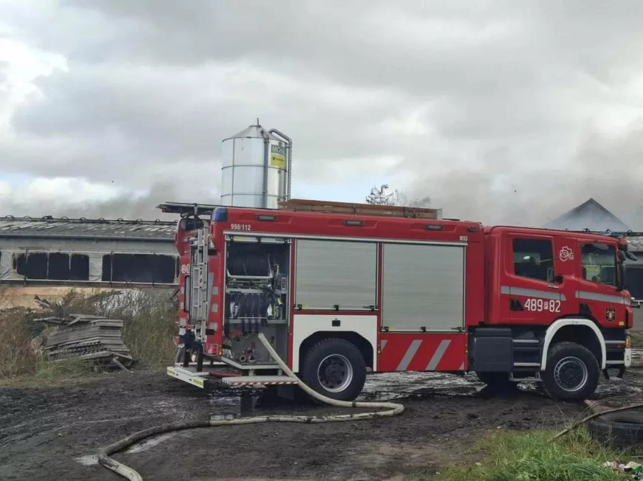 Wóz strażacki z rozwiniętą linią gaśniczą przed palącą się oborą