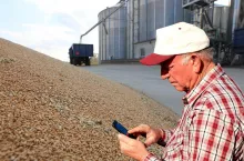 Rolnik patrzący w telefon stojący w skupie zbóż