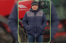 Rolnik w kurtce i czapce stojący przed ciągnikiem rolniczym