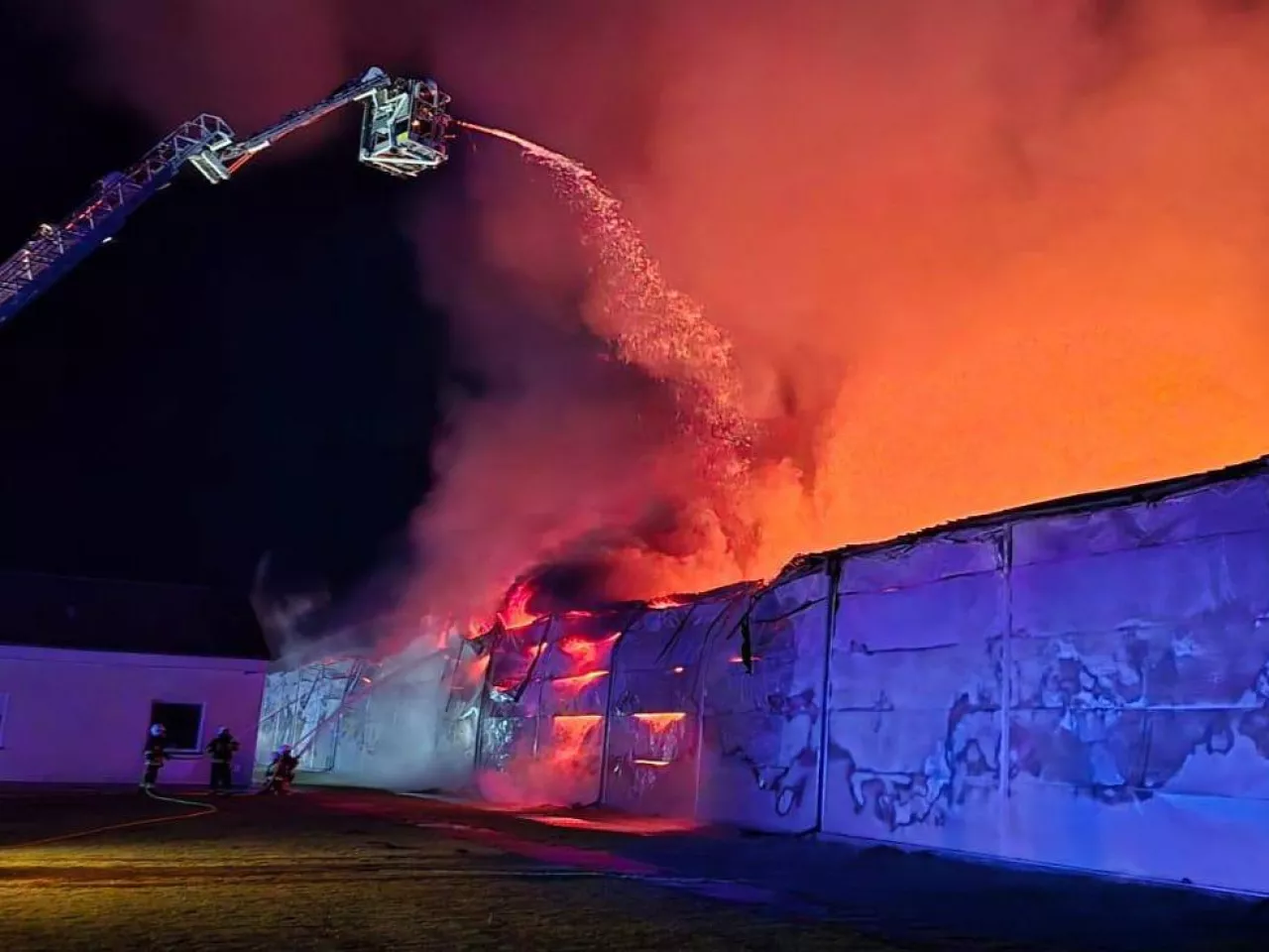 Strażacy z podnośnika polewają palący się budynek kurnika