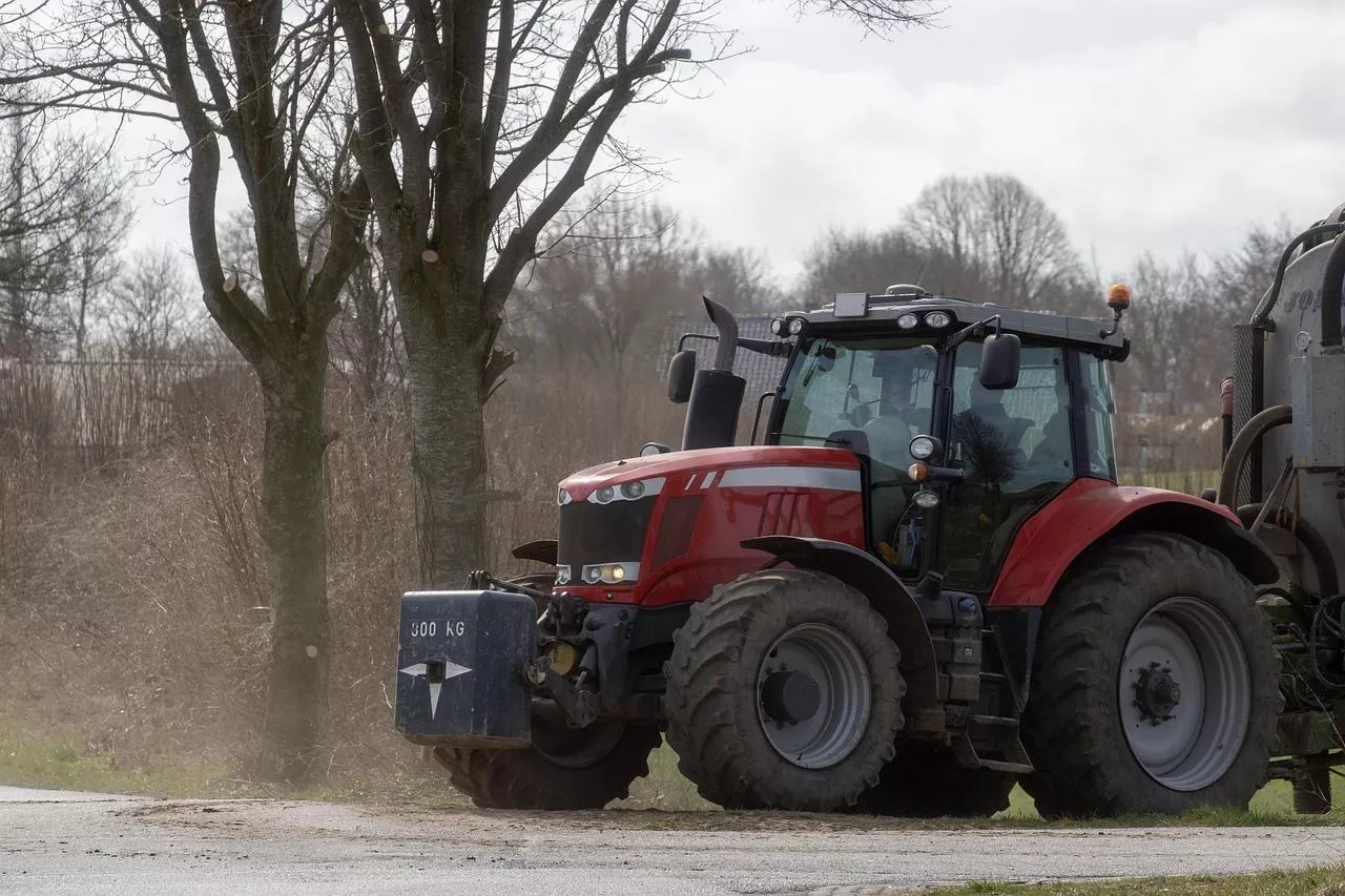 Czerwony traktor z obciążnikiem z przodu poruszający się po drodze, ciągnąc za sobą maszynę rolniczą