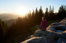 kobieta siedzi na skale w górach i patrzy na zachód słońca