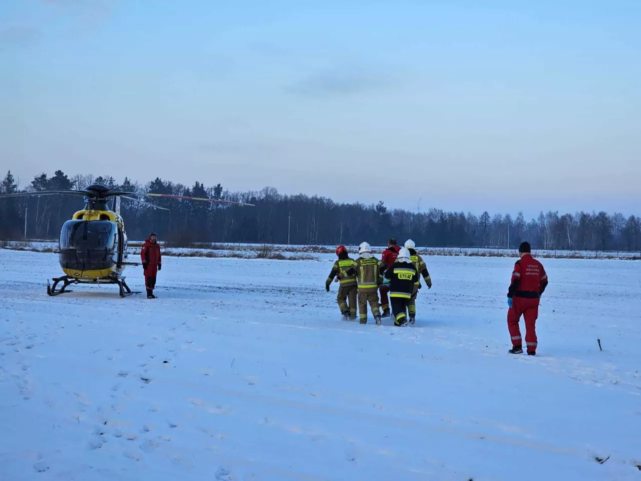 Strażacy na noszach przenoszą ranną kobietę do helikoptera LPR na polu w śniegu