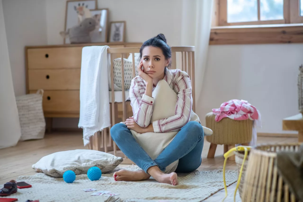 At home. Sad young woman hugging pillow, propping up her head, sitting on the floor