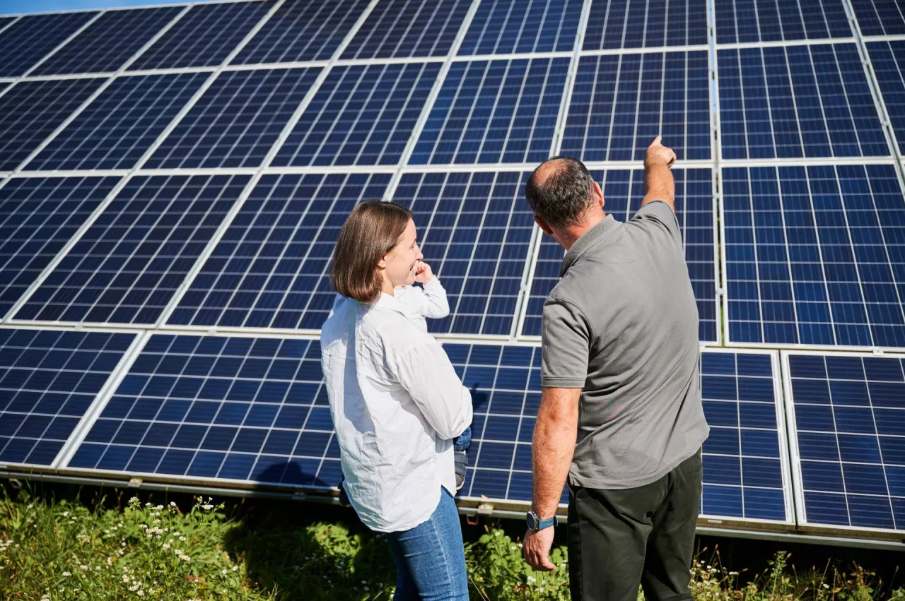 Happy father showing his wife and little son new solar panels. Young family getting acquainted with modern innovation. Back view of young woman with cute child and man looking at solar panels.